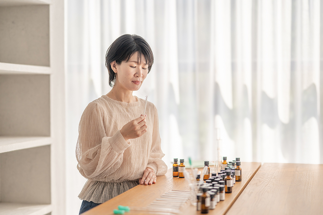 女性がムエットで香りを嗅いでいる様子。机の上にはたくさんの精油瓶